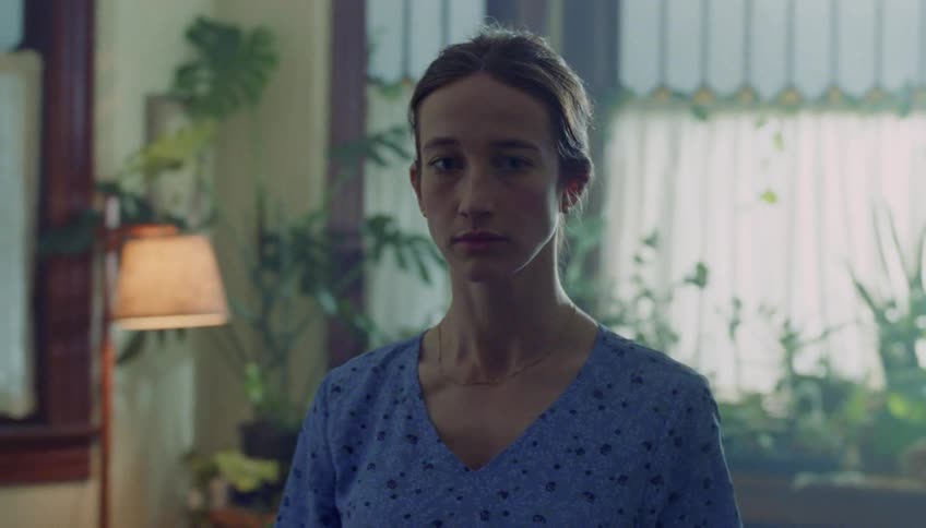Young adult woman wearing a blue dress walking in a room looking around indoors during day time