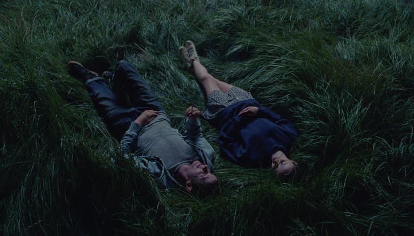 Two people lying in the tall grass smoking