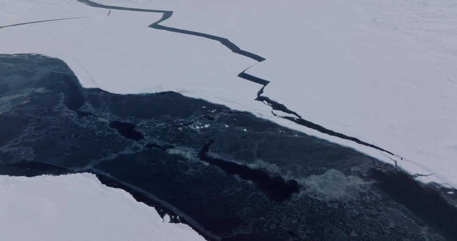Irregular crack cuts through the ice surface revealing dark water below