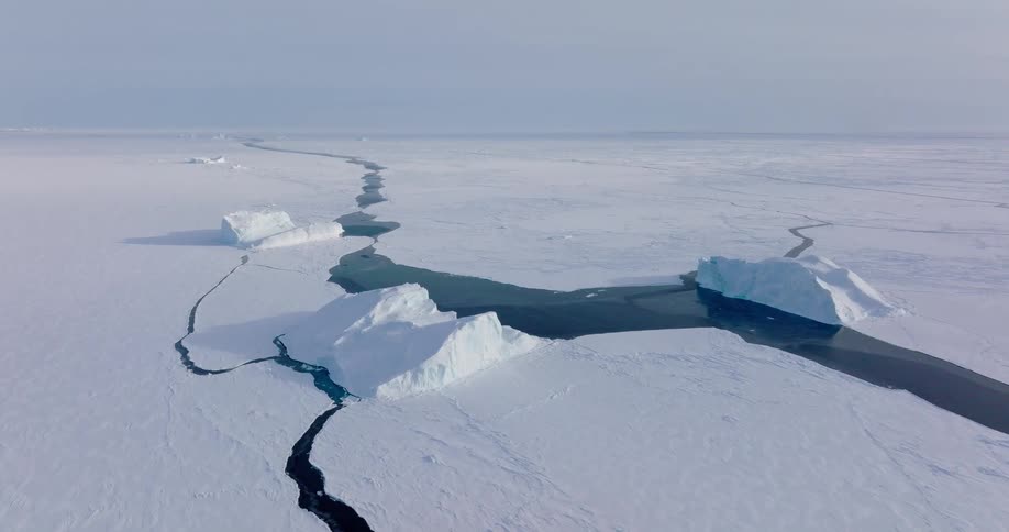 Cracks in sea ice form dark water channels between frozen blocks in a polar landscape