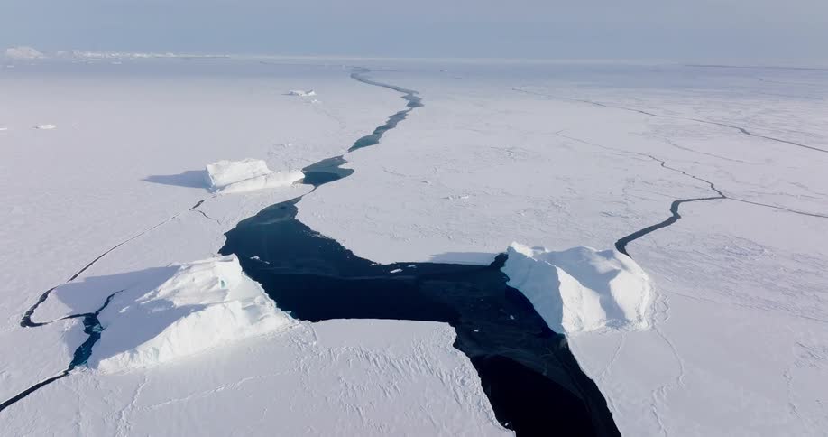 Aerial view of a large crack running through a frozen arctic ice sheet with dark ocean beneath