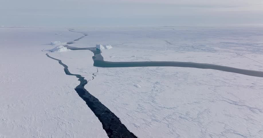 Aerial view of a dark blue lead of water cutting through a vast frozen arctic ice shelf