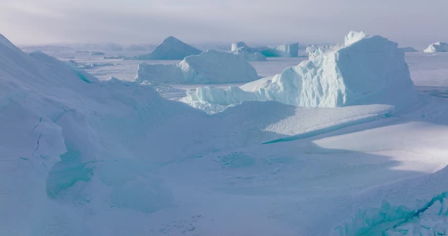 Icebergs with angular formations rise above frozen water in a polar landscape
