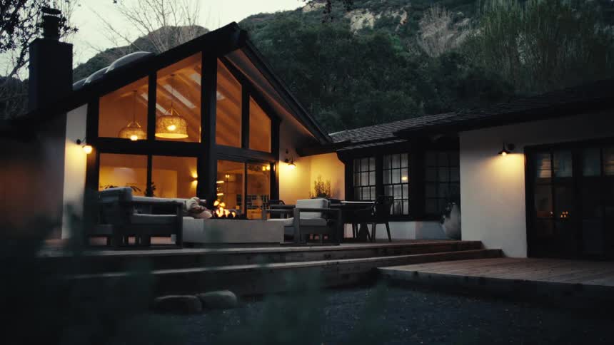 A person relaxing on a modern patio outside a mountain house at dusk