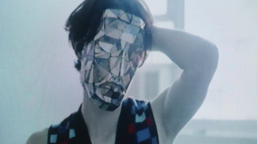 A woman wearing a mirrored mask is running her hand through her hair