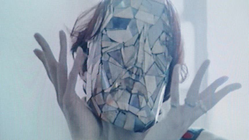 Face covered by a geometric mask with a fragmented pattern under cool backlighting