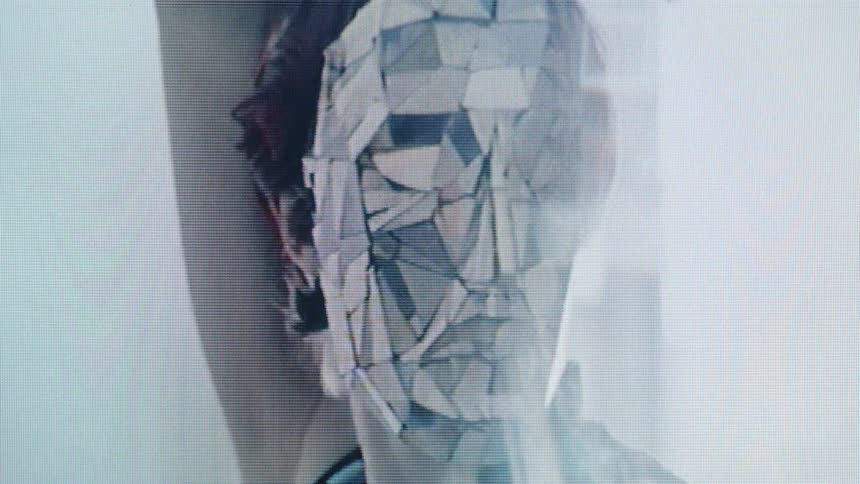 A fragmented glasslike human face overlays a real head creating an abstract futuristic image that suggests identity breaking apart or transforming