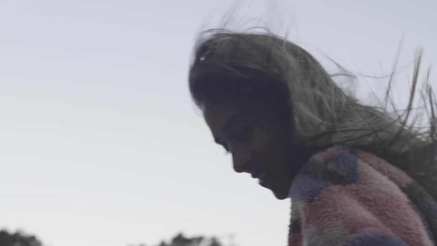 A smiling woman leans out of a car sunroof with the wind blowing through her hair