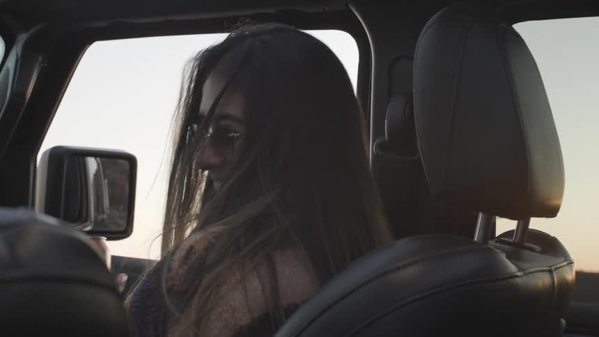 Woman sitting in an automobile laughs as the man in the drivers seat touches her head and she pushes her hair back with her hand