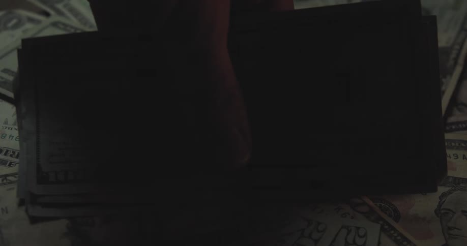 Hand grabbing dollar bills from a surface covered with money