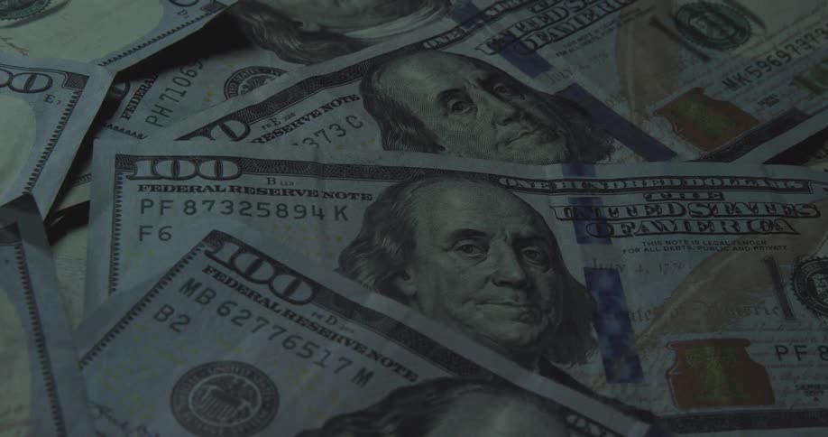 Stacks of 100dollar bills lie on an indoor surface arranged in neat bundled piles