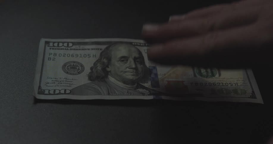 Person picking up a dollar bill from a dark surface