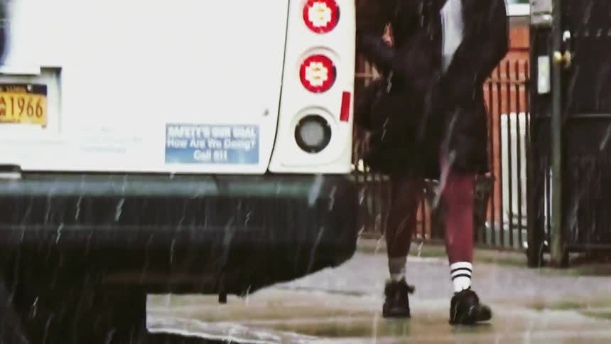 Pedestrians walk along a city sidewalk and cross the street behind a white vehicle during a heavy rainstorm the lowangle shot captures peoples legs and footwear as they navigate the wet pavement and puddles