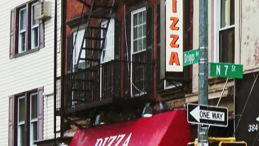 People picking up and carrying things on the sidewalk in front of a pizza place in an urban area under snow outdoors during day time