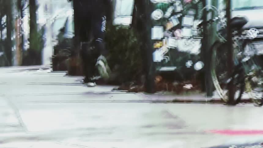 A person wearing black clothes and white sneakers runs away from the camera along a wet sidewalk in a city during a rain storm