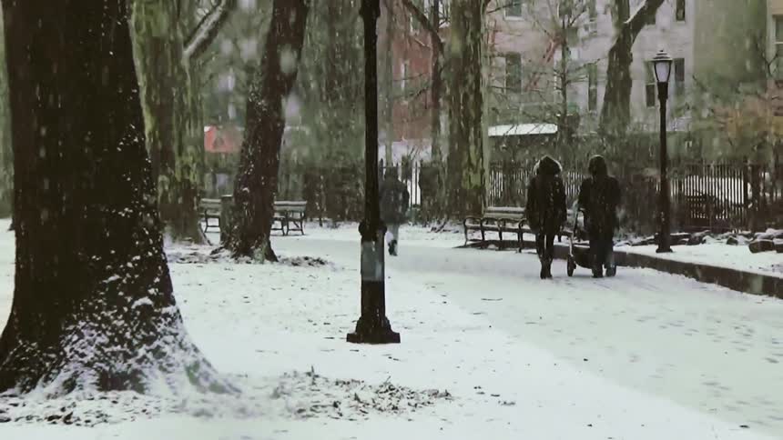 People walking through a snow covered beautiful park with trees and benches
