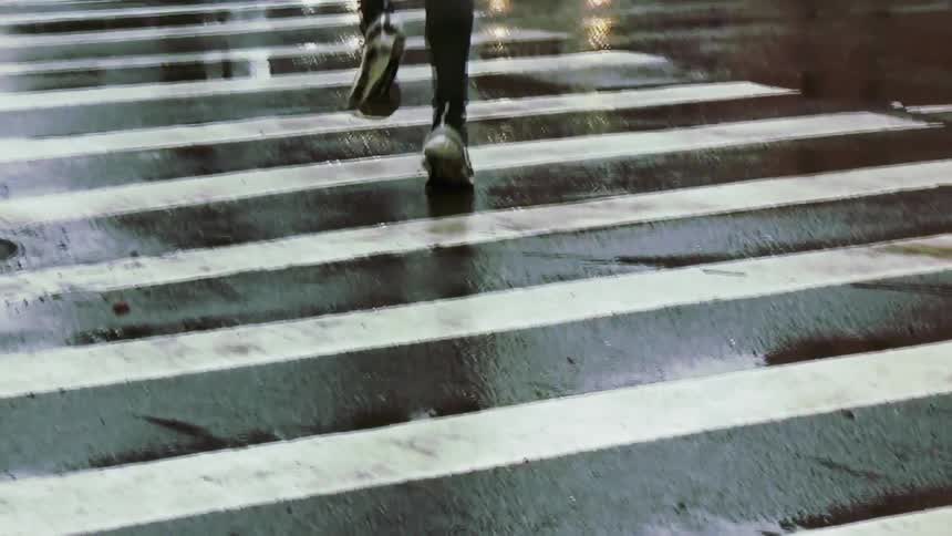 Runner and a pedestrian cross a wet intersection while cars wait on a winter day