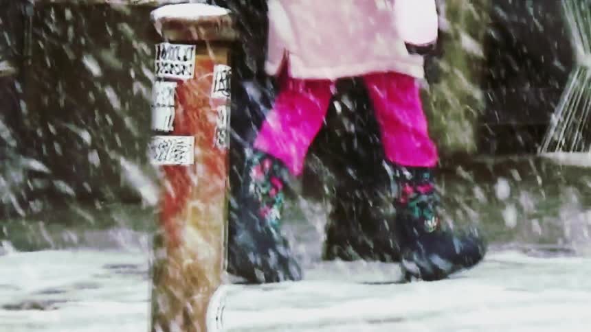Person walking during snowfall in an urban area with benches in the background