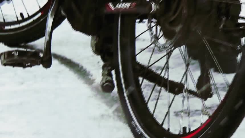 A person tries to ride a bike in the snow on a snowy day struggling to get it moving through the thick slippery ground