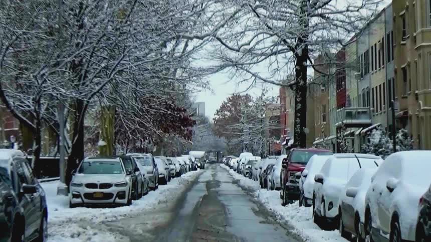 Snow covered cars parked on the street in front of apartment buildings on a winter day