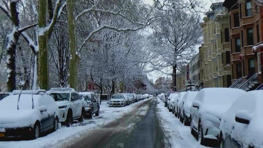 A quiet residential street with brownstones and parked cars blanketed in fresh winter snow