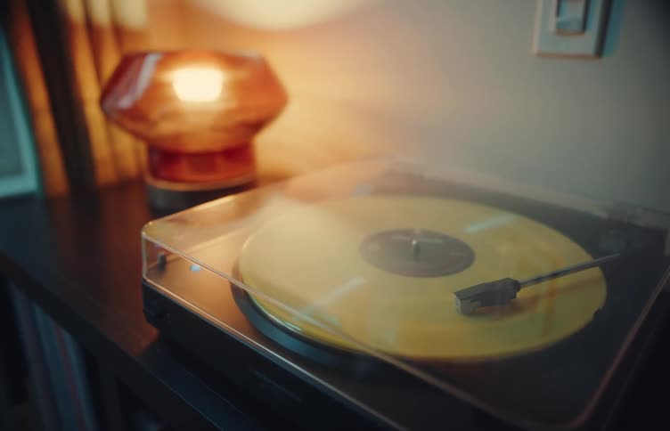 Turntable with a yellow vinyl record on a cabinet beside a lit lamp