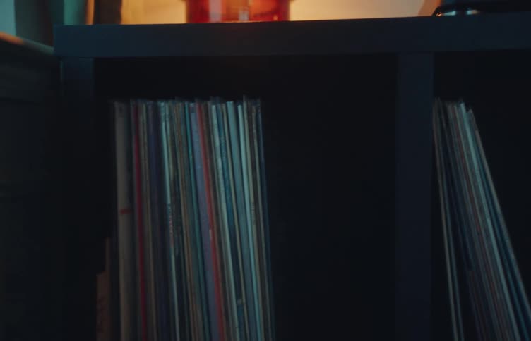 Shelf with vinyl records turntable and a lit lamp in the background