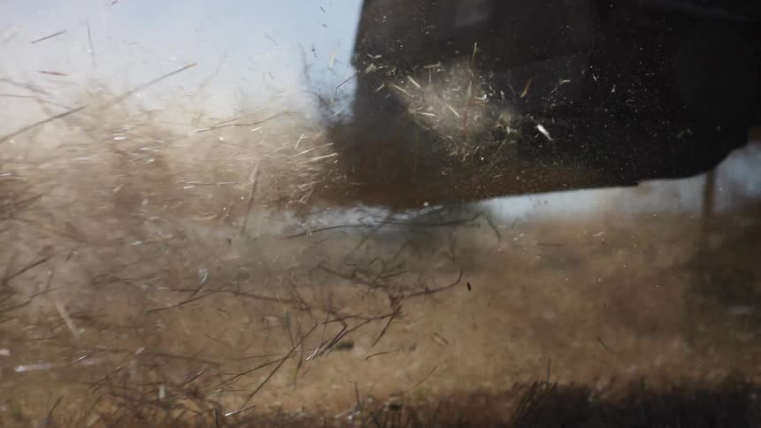 Straw and dirt burst into the air as farm machinery moves over dry ground during harvest