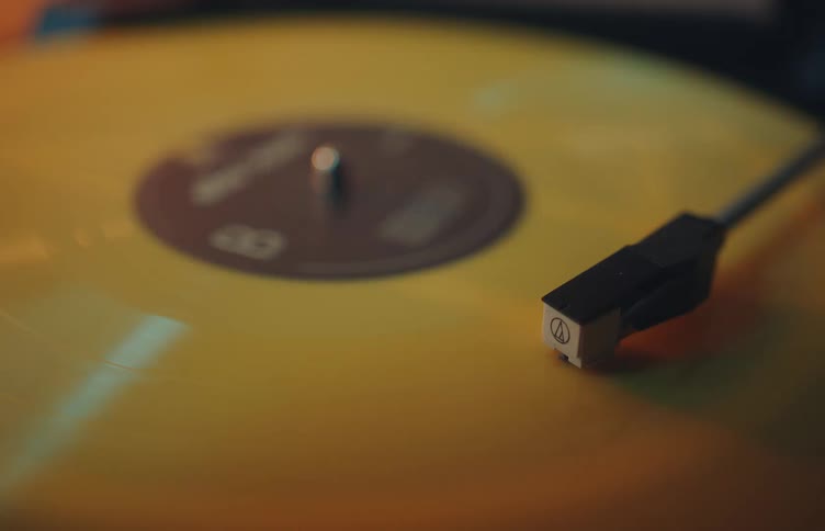 Turntable needle positioned on a yellow vinyl record during playback