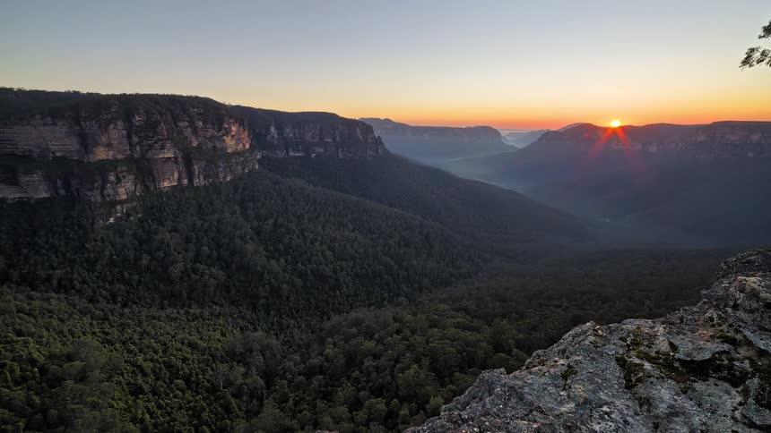 Aerial view of a mountain valley with warm light over dense forests and distant ridges at sunset