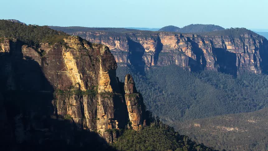 The first is a sharp vertical cliff edge in the foreground that catches the golden light of the sun creating a highcontrast boundary against the dark shadows of the valley behind it a second line is formed by a slender rock spire or pinnacle that sta
