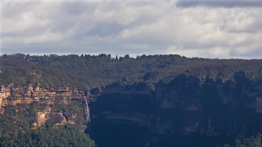 Forest around mountain canyons as a waterfall flows over the cliff