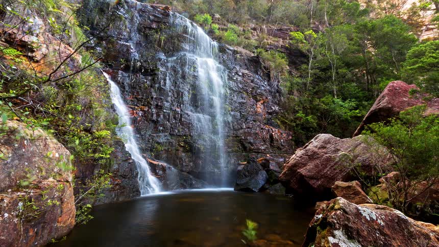 Waterfall flowing down a rocky cliff into a natural pool surrounded by vegetation