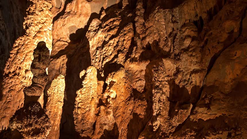 Warm light illuminates the rough rock formations casting shadows on the textured walls of a natural cavern