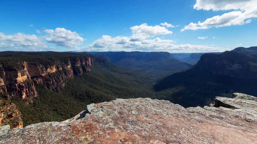 Rocky lookout with a wide view of a vegetationcovered canyon under a blue sky