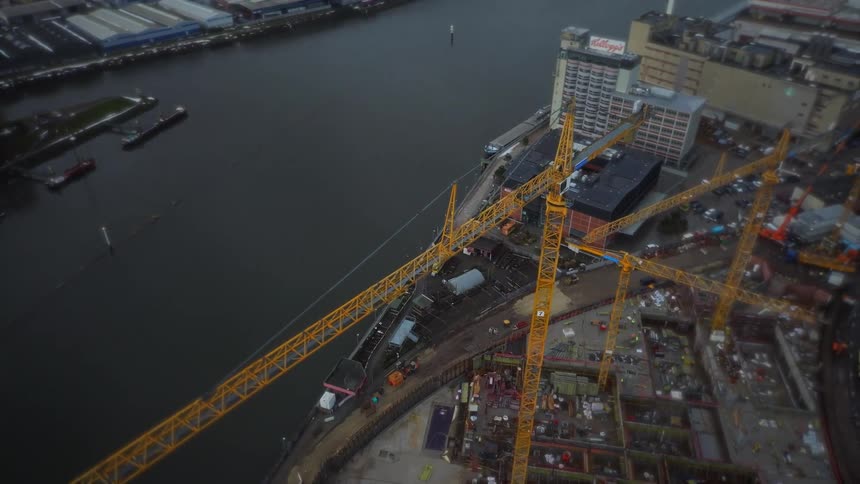 Tall yellow construction cranes stand near the waterfront of a city in the winter