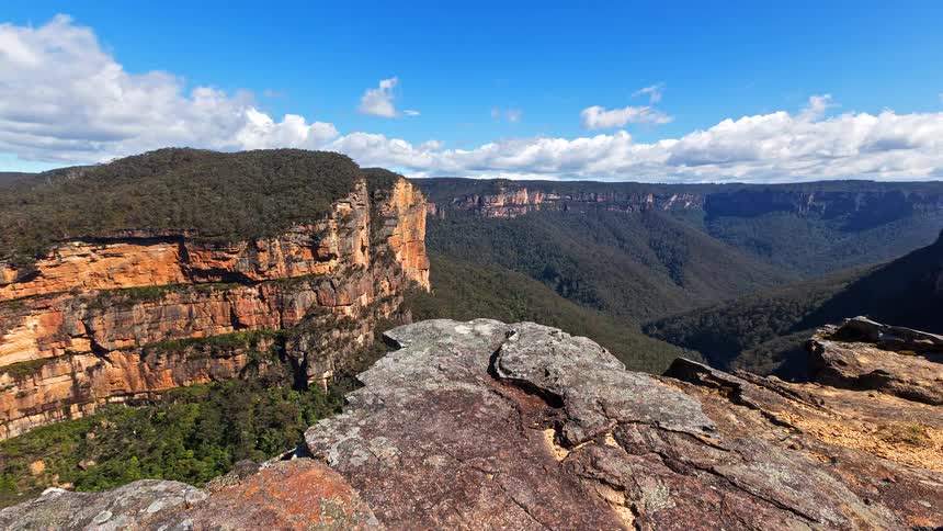 View of forested canyon from rocky cliff under blue sky with clouds