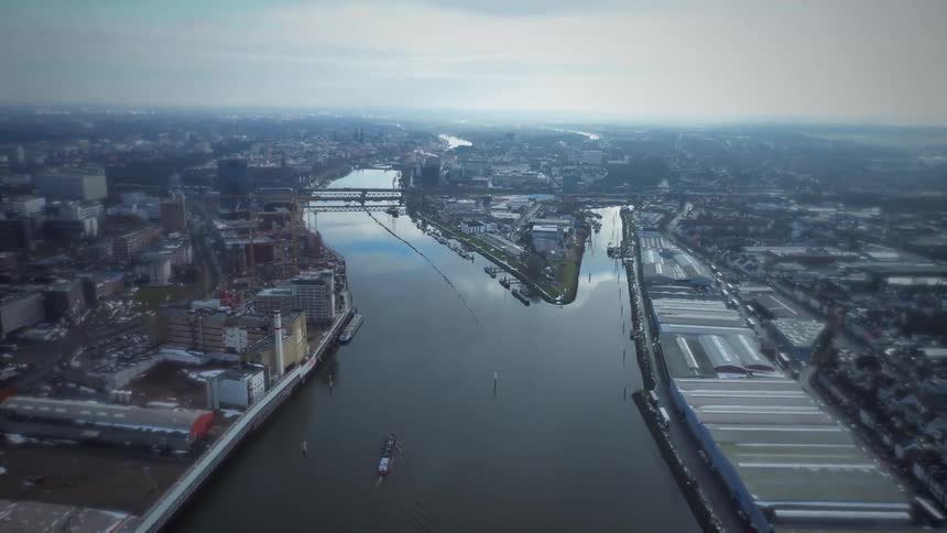 An aerial view shows a wide river flowing through a large city with many buildings and bridges under a cloudy sky during the day