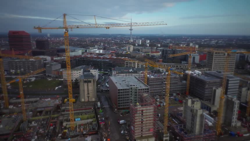 Aerial view of an urban construction zone with cranes and unfinished buildings across a dense city