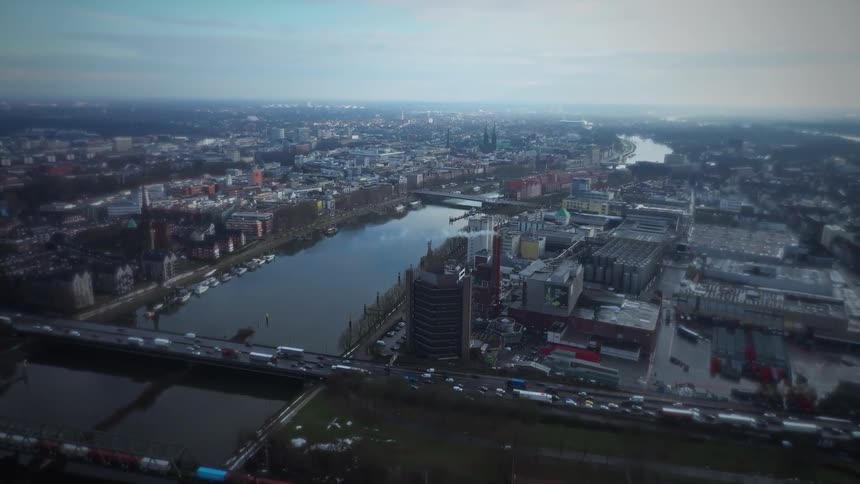 An aerial view shows a wide river flowing through a large city with many buildings and bridges under a cloudy sky during the day