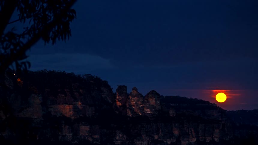A bright orange full moon rising behind a rugged rock formation at night