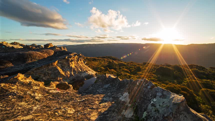 Sun setting over a mountainous landscape seen from a rocky lookout