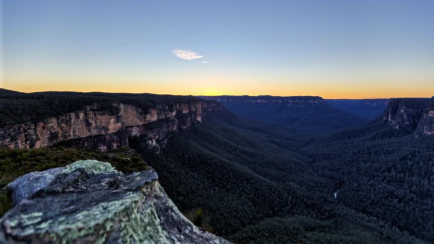 Cliffs overlook a forested mountain valley as shadows move across the landscape with the setting sun