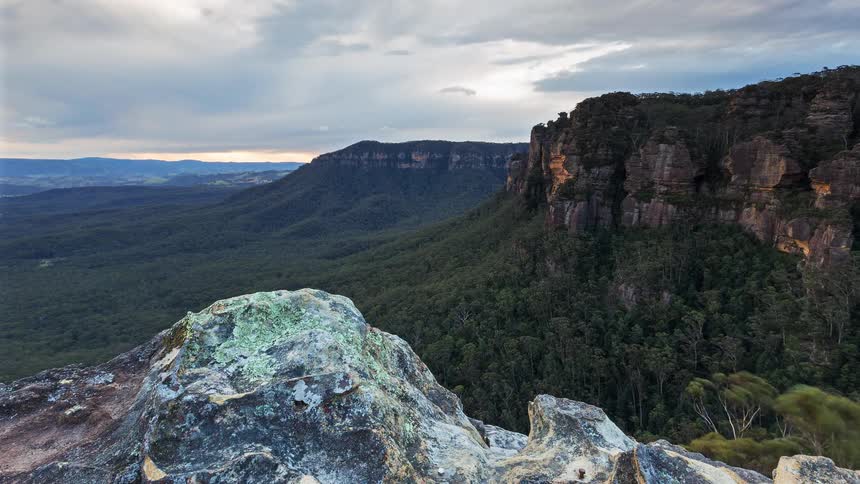 From the peak of a rocky mountain a view of grasscovered wilderness with hills and a mountain range from daylight to sunset