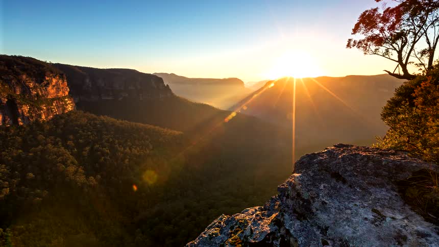 Sun rising over a vegetationcovered canyon seen from a rocky lookout
