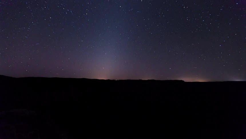 A time lapse shows the sun setting over a deep valley with rocky cliffs before the sky turns dark and reveals the stars above moving clouds during the night