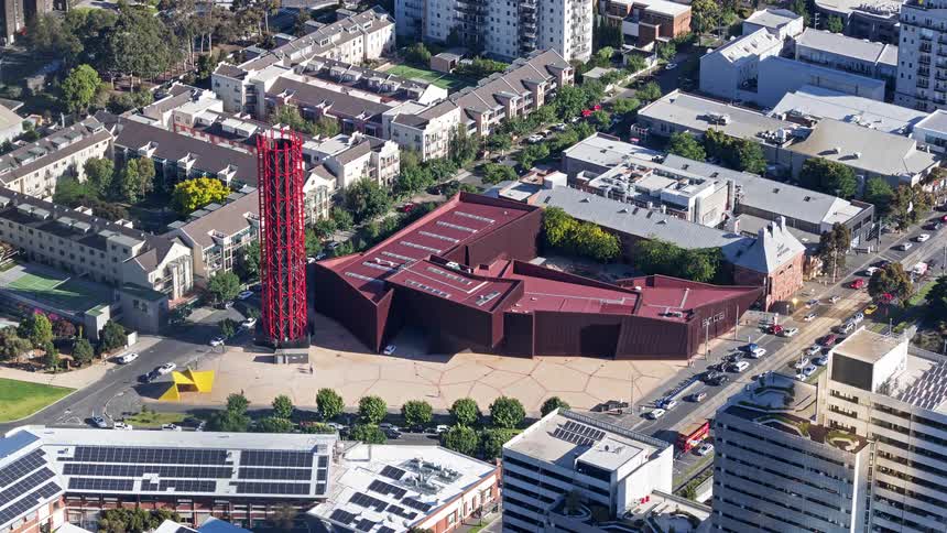 An aerial view shows angular rust colored buildings and a red tower in a city