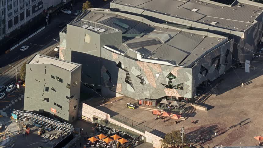 People walk outside of a large building with asymmetrical architecture