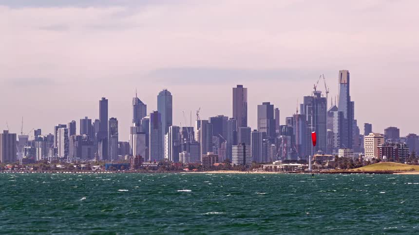 People paraglide above the coastline with colorful parachutes soaring against a city skyline
