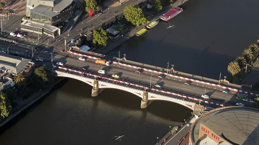 Aerial view of cars and a tram crossing a busy city bridge over a river in a dense urban area
